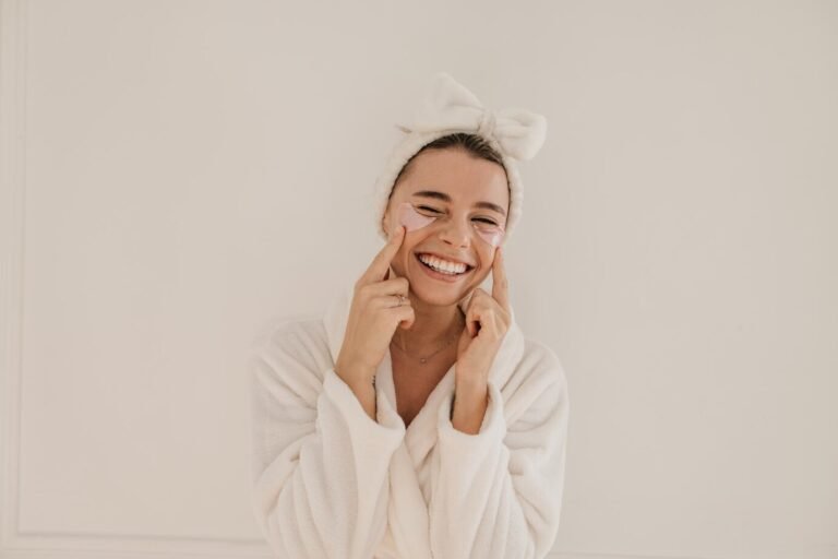 smiling-young-caucasian-woman-terry-bathrobe-squints-applies-transparent-patches-eyes-white-background-home-spa-facial-concept_197531-31559